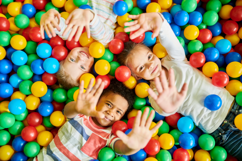 View from above of three kids laying down in a ball pit smiling