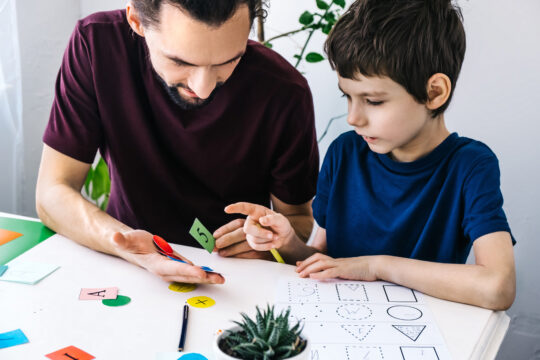 A man and a young boy interact using numbers and letters on colorful pieces of paper